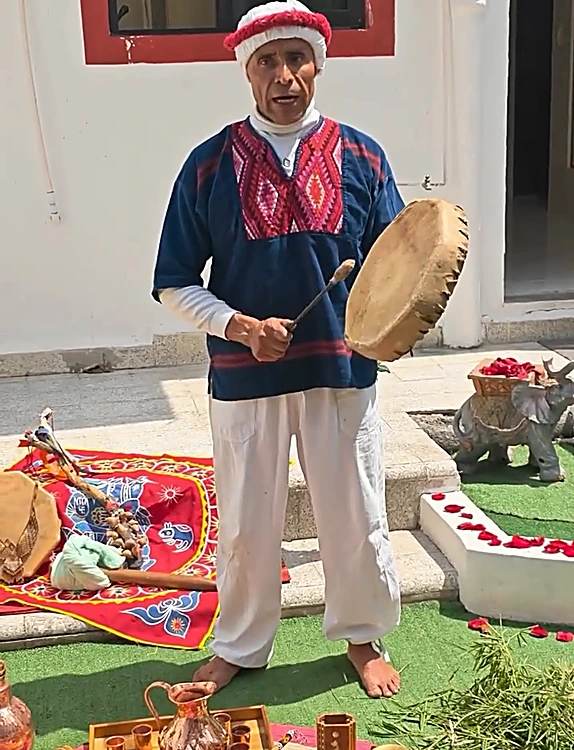 El guía del temazcal toca el tambor en el jardín, junto a la ofrenda y un petate bordado