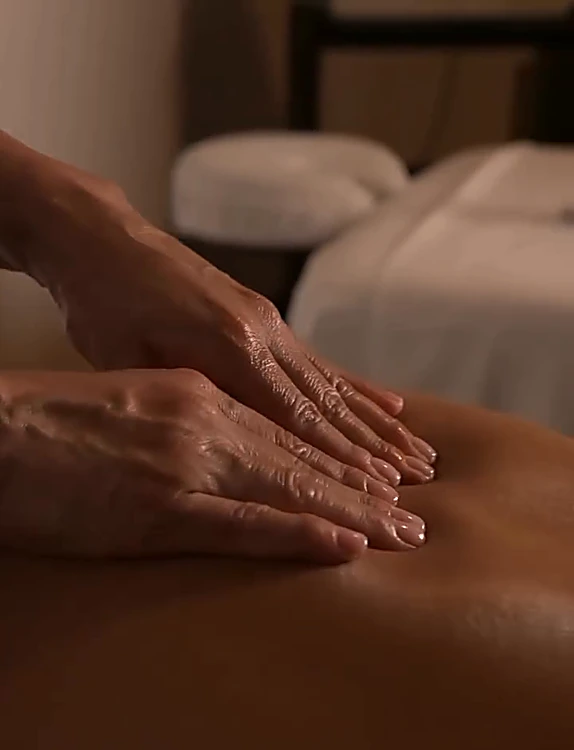 Manos de una terapeuta dando masaje en la espalda, con la luz cálida de la cabina