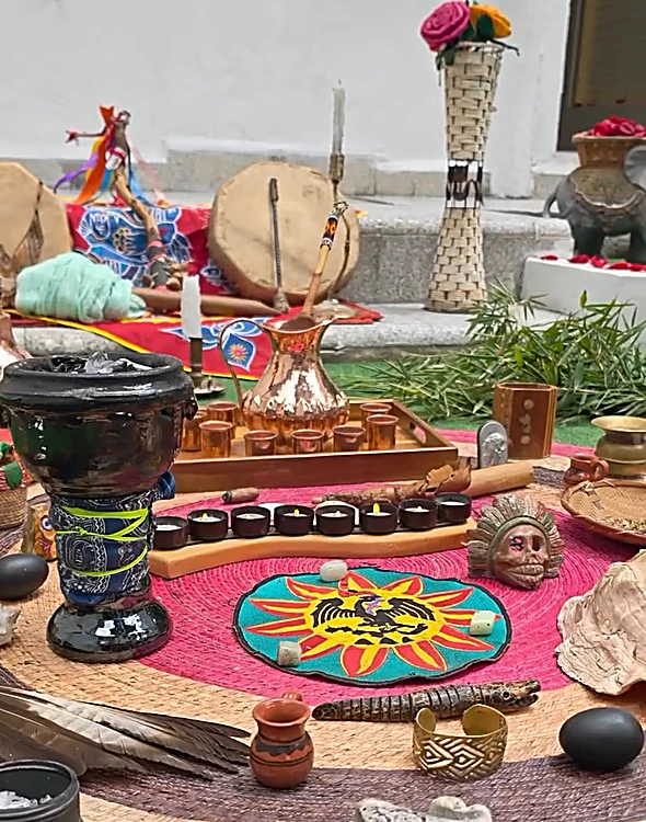 La ofrenda del temazcal sobre un petate rosa: sahumador de copal, tambores, velas, plantas y un disco con el sol y el águila