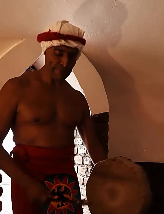 El guía toca el tambor dentro del temazcal, bajo la bóveda blanca iluminada en tono cálido