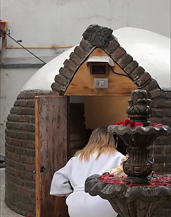 El temazcal de Sukhavati: cúpula blanca sobre base de ladrillo, puerta de madera y una fuente de piedra con pétalos de rosa